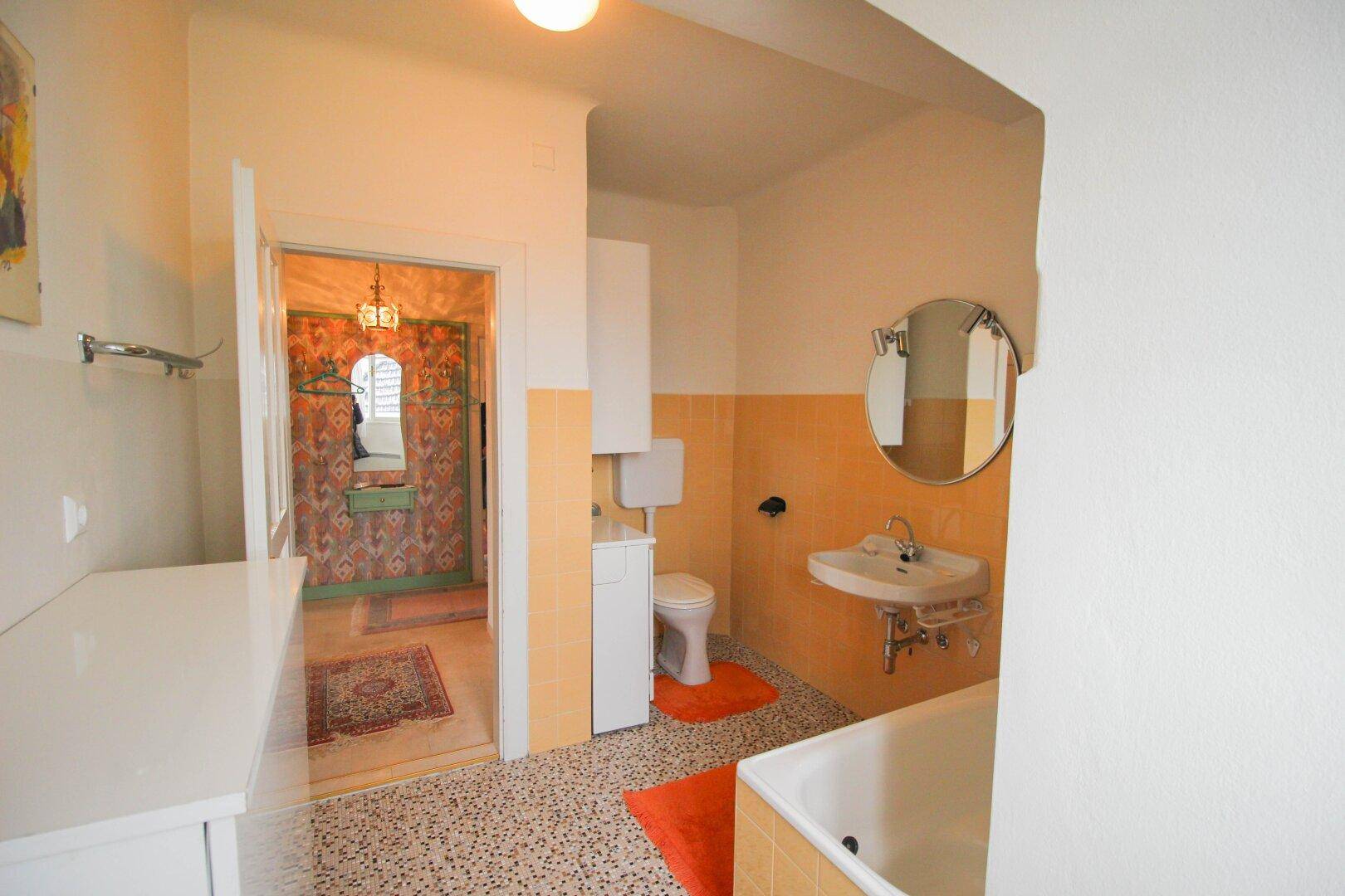 Badezimmer mit gelben Fliesen, Badewanne, Waschbecken und Terrazzoboden.