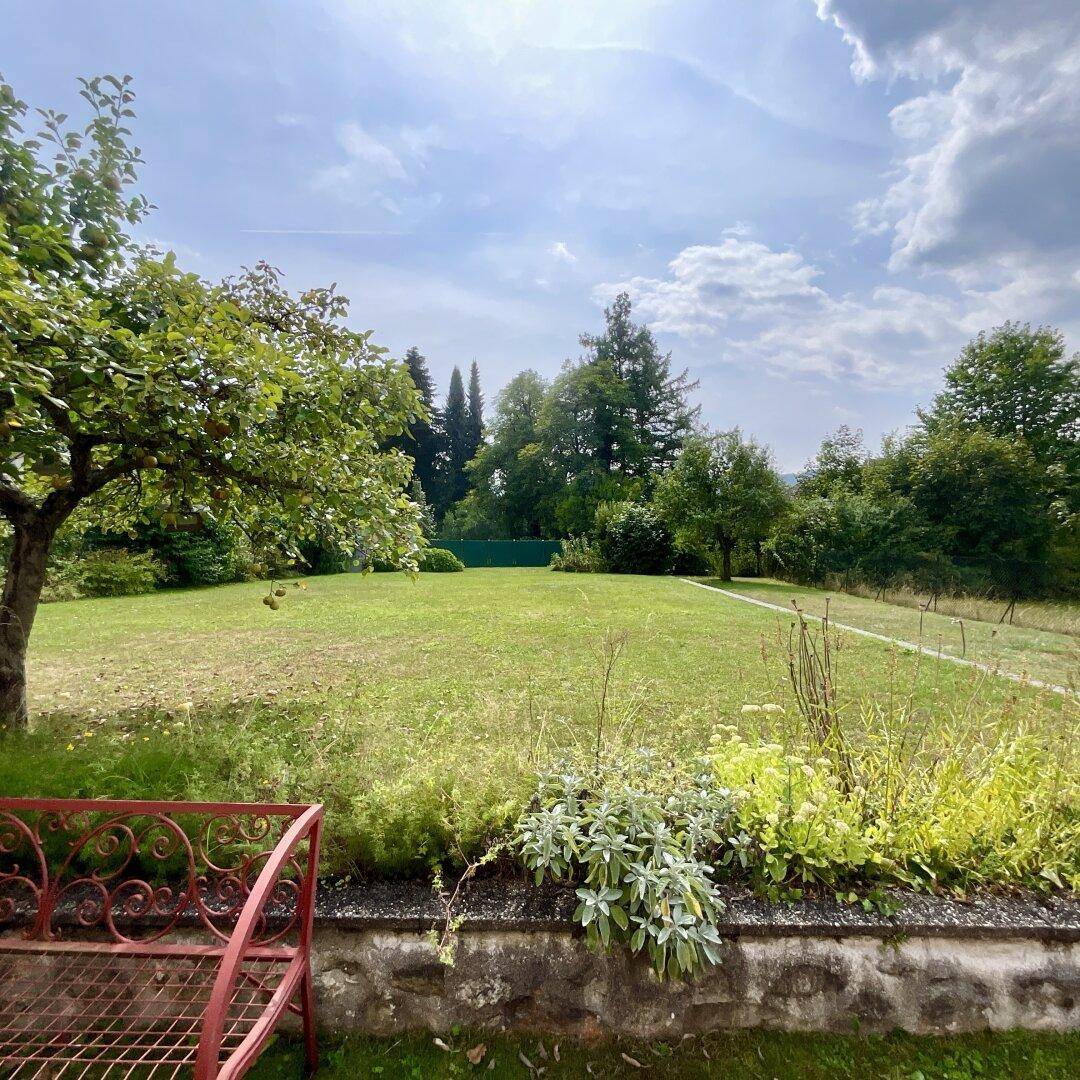 Weitläufiger Garten mit altem Baumbestand, Rasenfläche und einer roten Gartenbank.