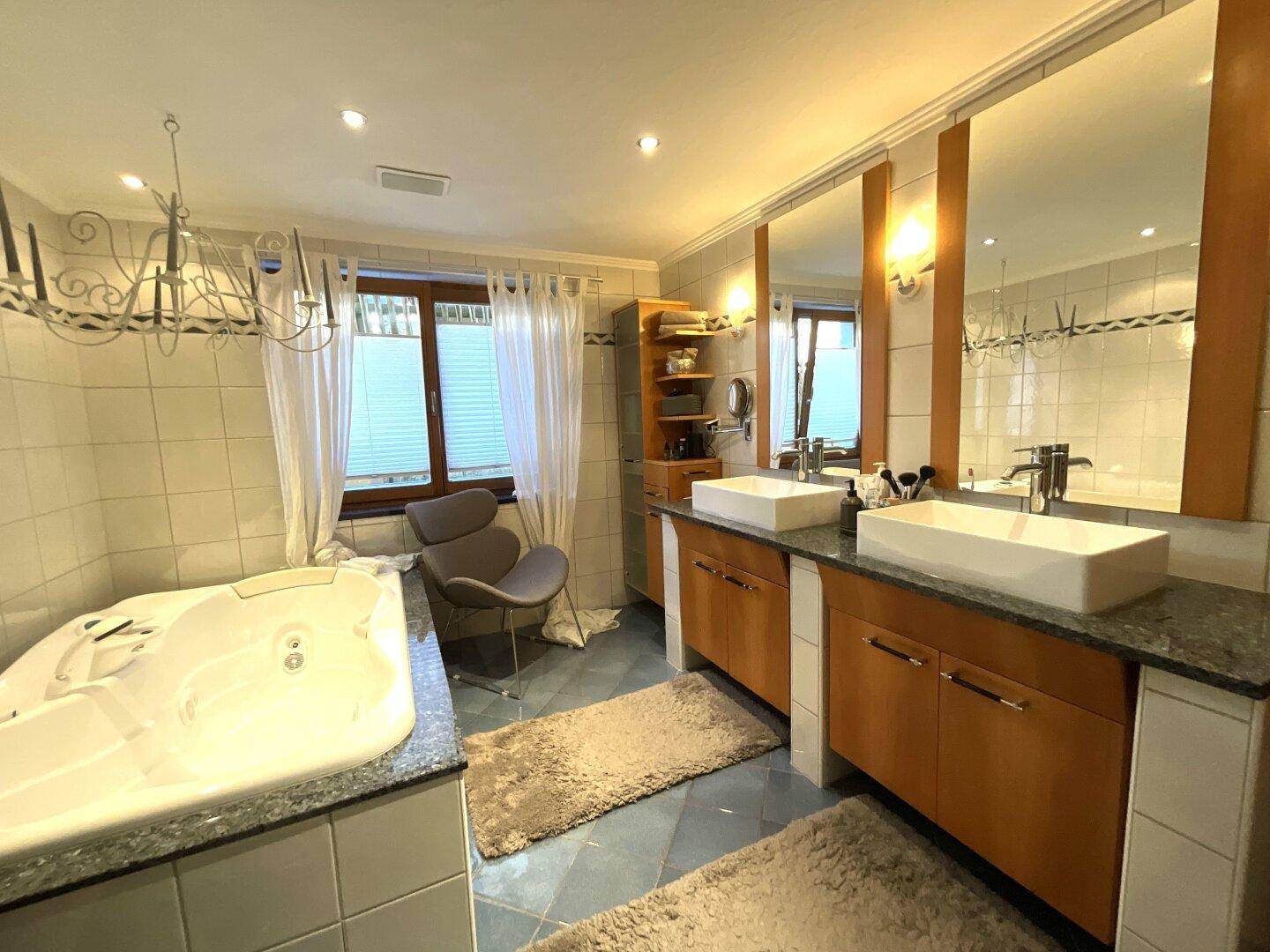 Geräumiges Badezimmer mit Doppelwaschbecken, Whirlpool-Badewanne und großen Spiegeln.