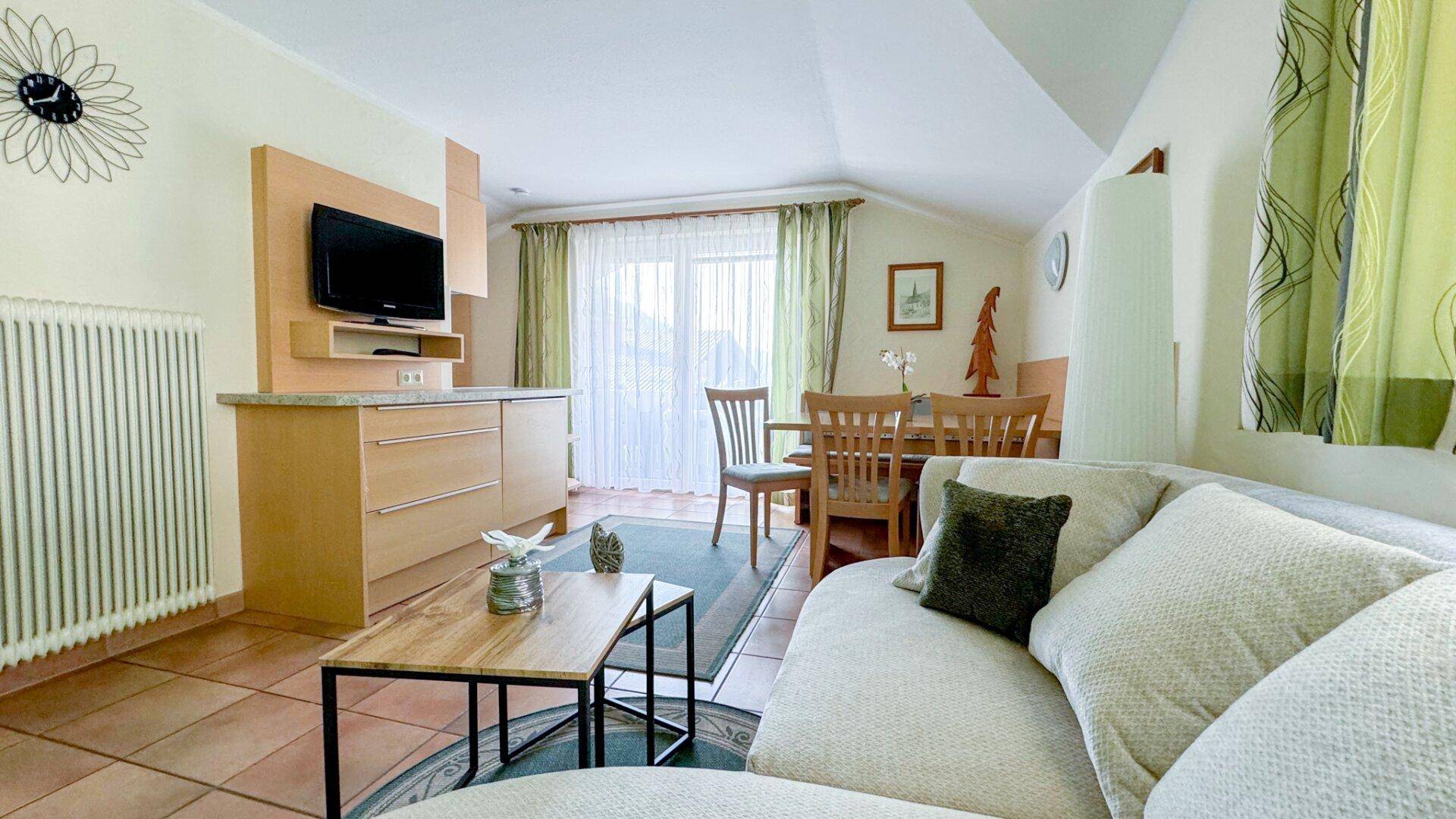 Gemütlicher Wohn-Essbereich mit Küchenzeile, Sofa und Zugang zu einem Balkon.