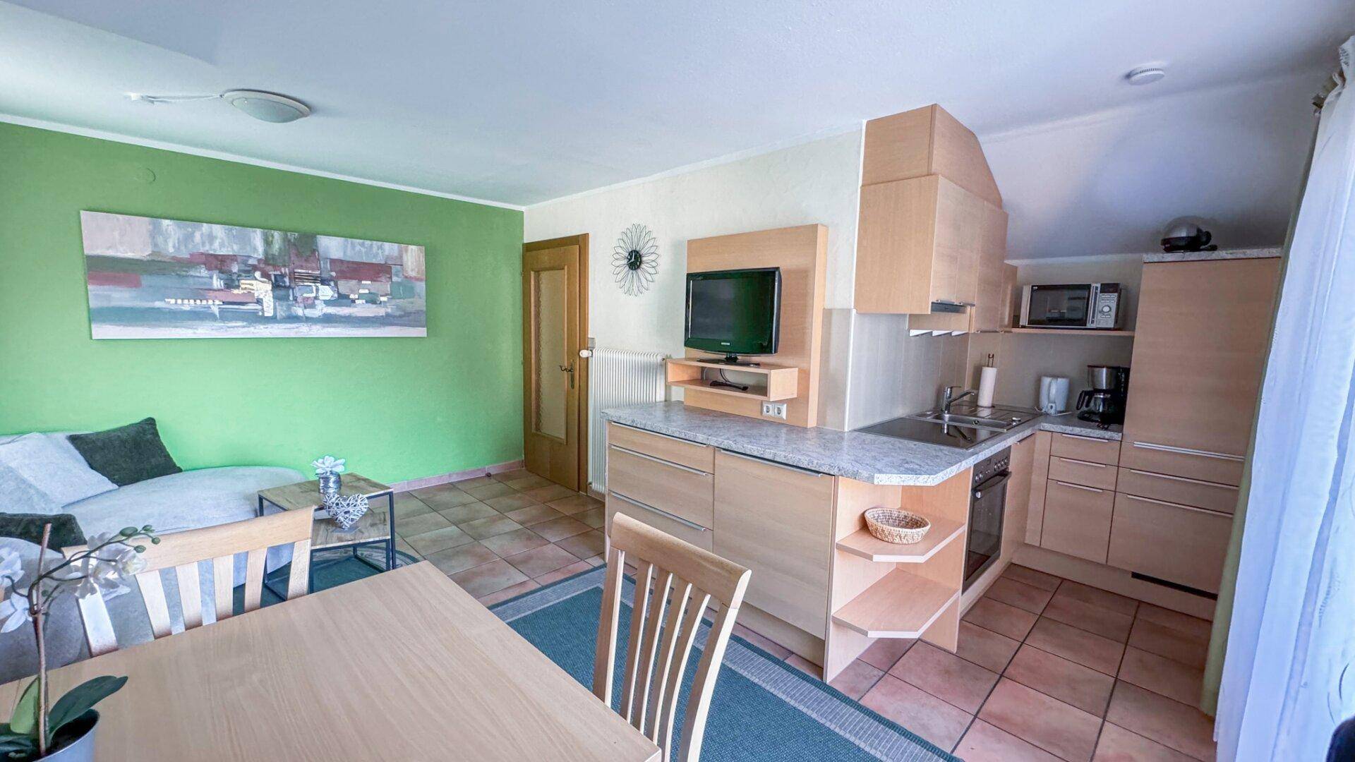 Heller Wohn-Essbereich mit grüner Akzentwand, Küchenzeile und Esstisch.