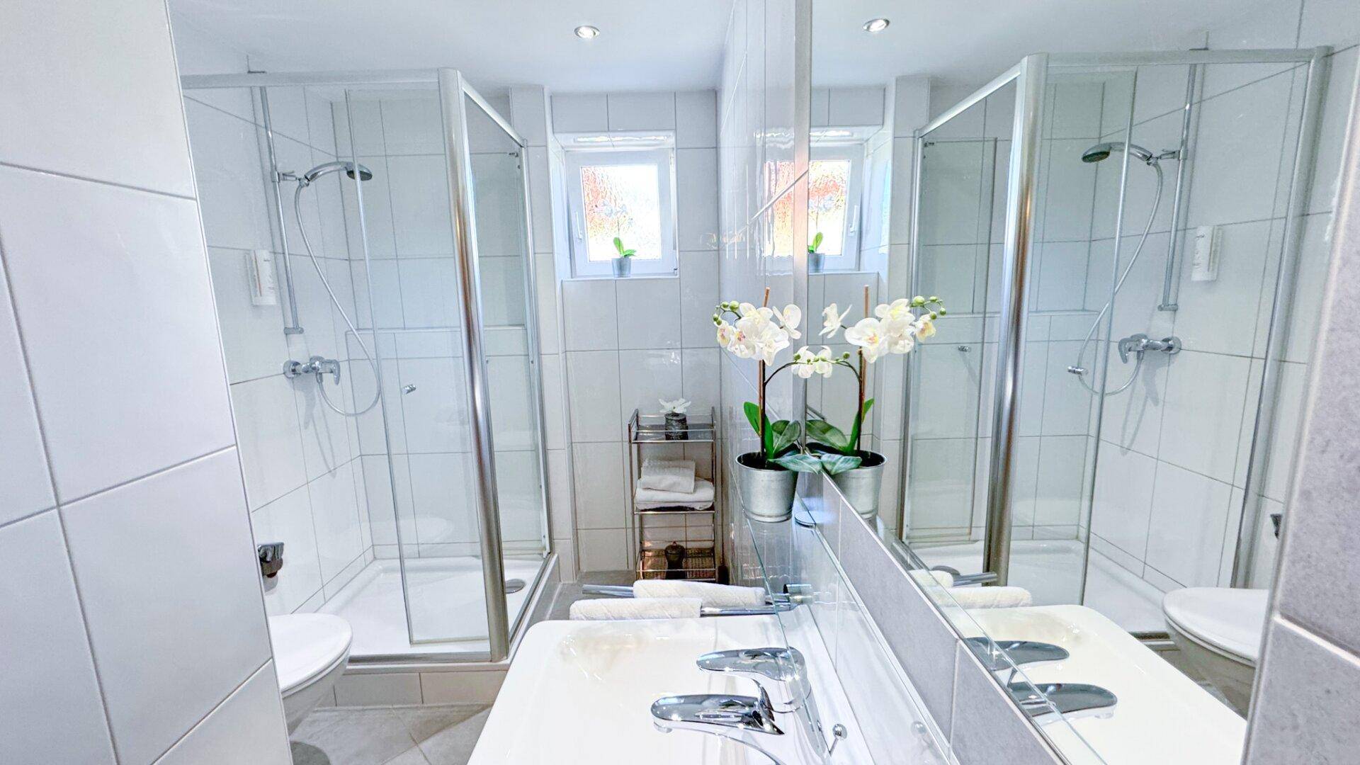 Modernes Badezimmer mit zwei Duschkabinen, Doppelwaschbecken und großen Spiegeln.