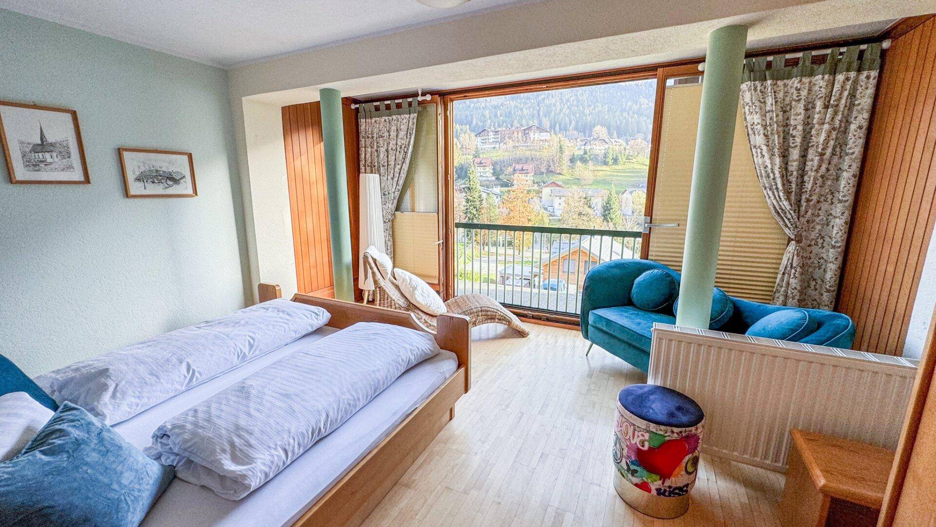Helles Schlafzimmer mit zwei Einzelbetten, Sitzgelegenheit und Balkonzugang mit Bergblick.