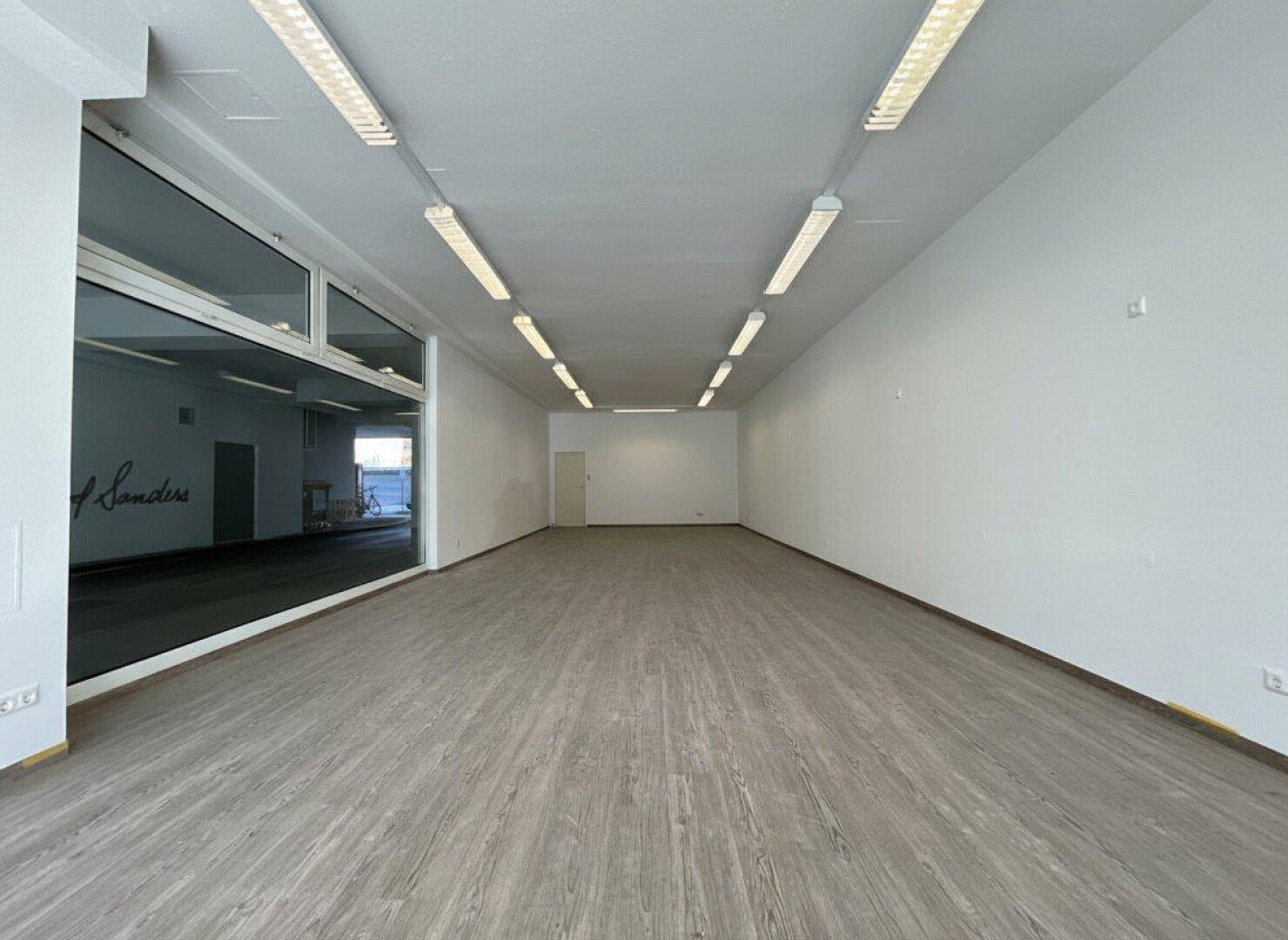Geräumiger Geschäftsraum mit weiß gestrichenen Wänden, Laminatboden und Deckenbeleuchtung.