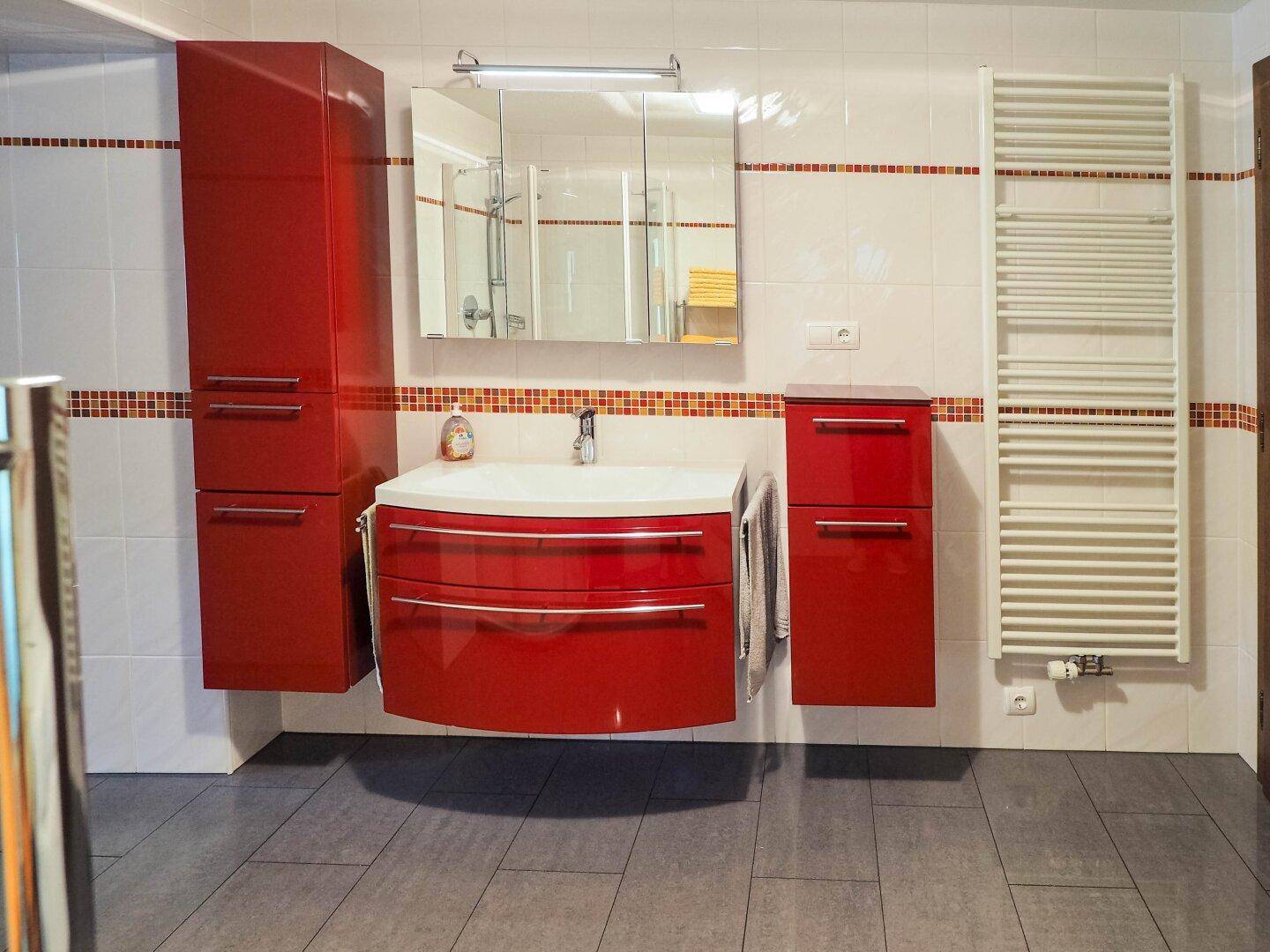 Modernes Badezimmer mit roten Waschtischunterschränken, Einzelwaschbecken und beheiztem Handtuchhalter.