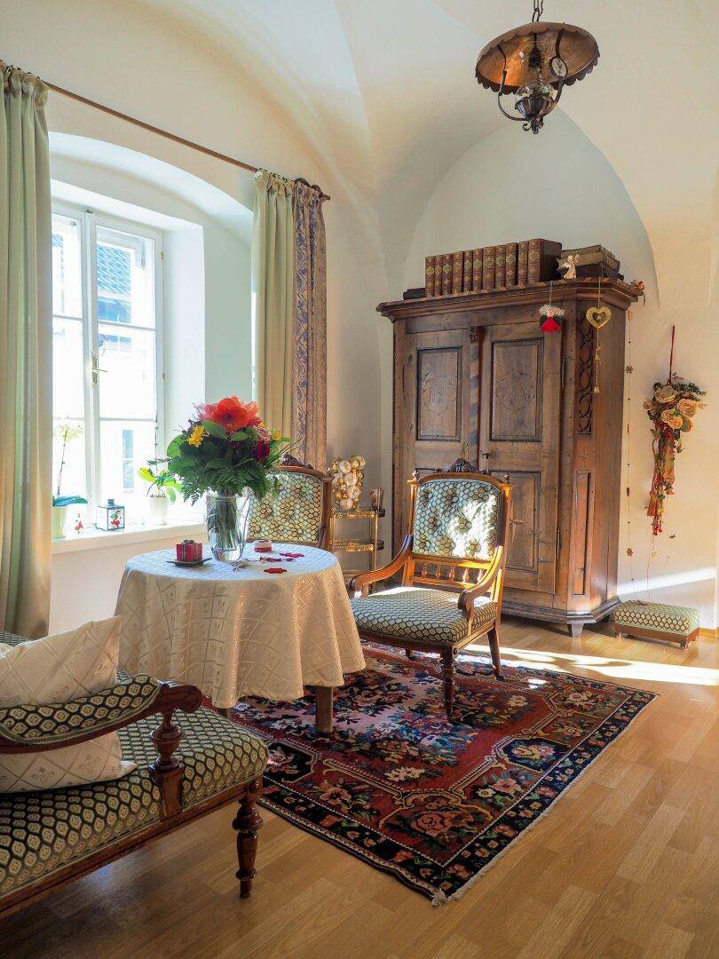 Historischer Raum mit Gewölbedecke, Holzboden, antiken Möbeln und einem kleinen runden Tisch am Fenster.