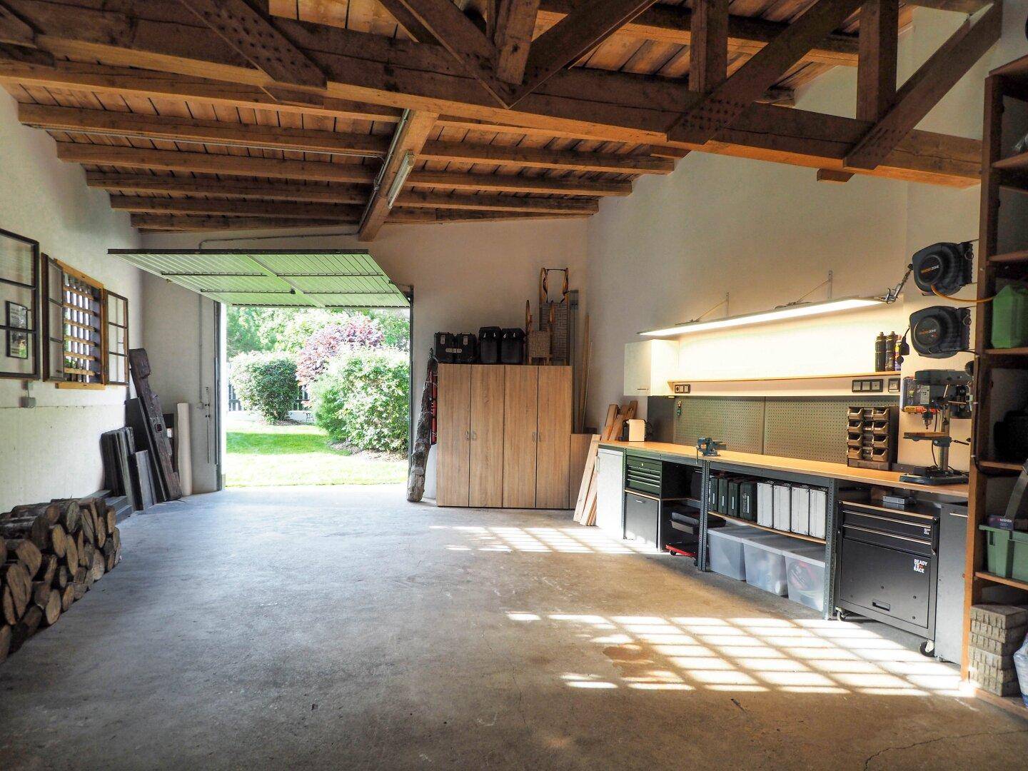 Geräumige Garage oder Werkstatt mit Betonboden, sichtbaren Holzdeckenbalken und Arbeitsbereich.
