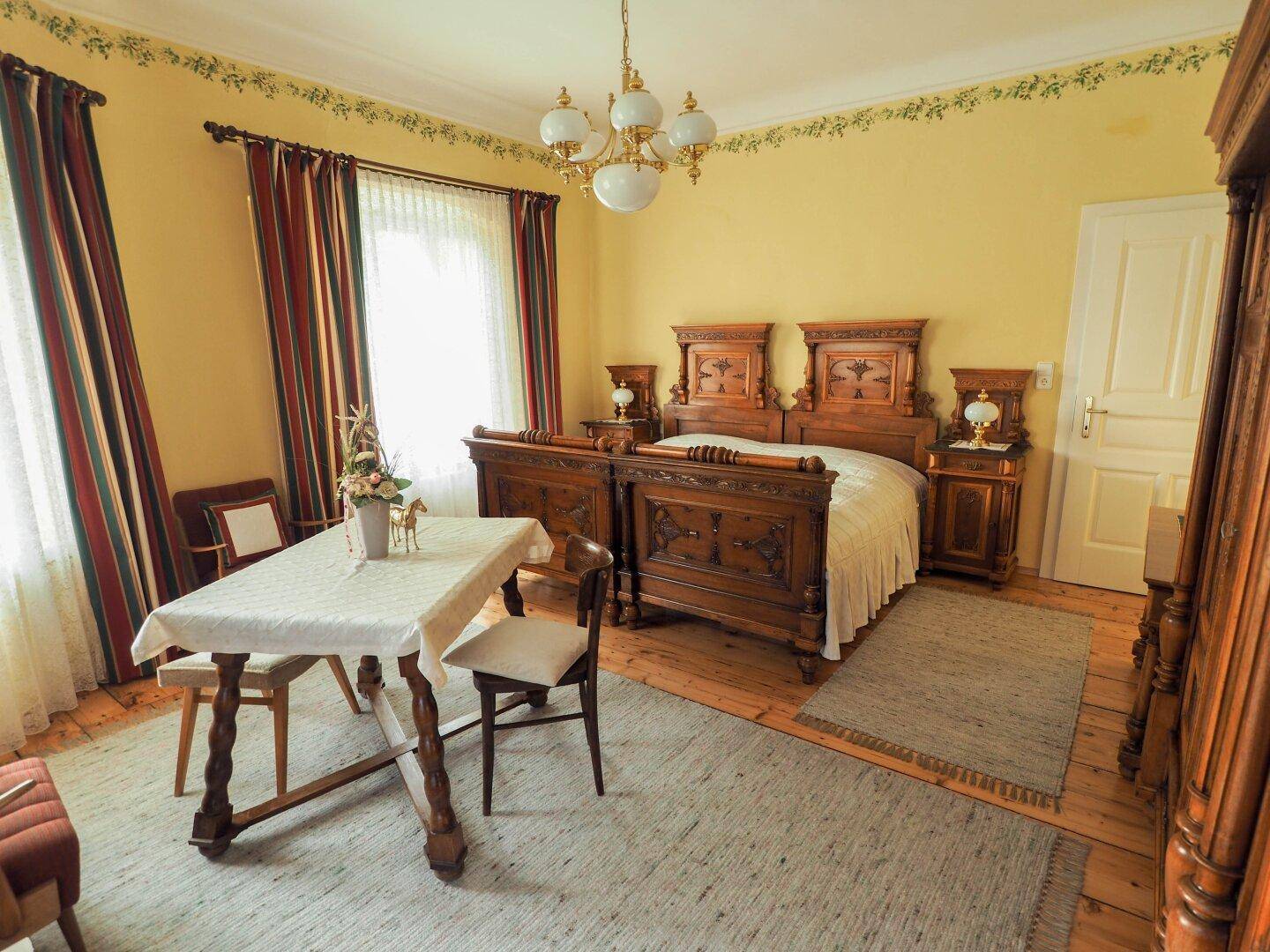 Geräumiges Schlafzimmer mit kunstvoll geschnitzten Holzbetten, Holzdielenboden und gelben Wänden mit floraler Bordüre.