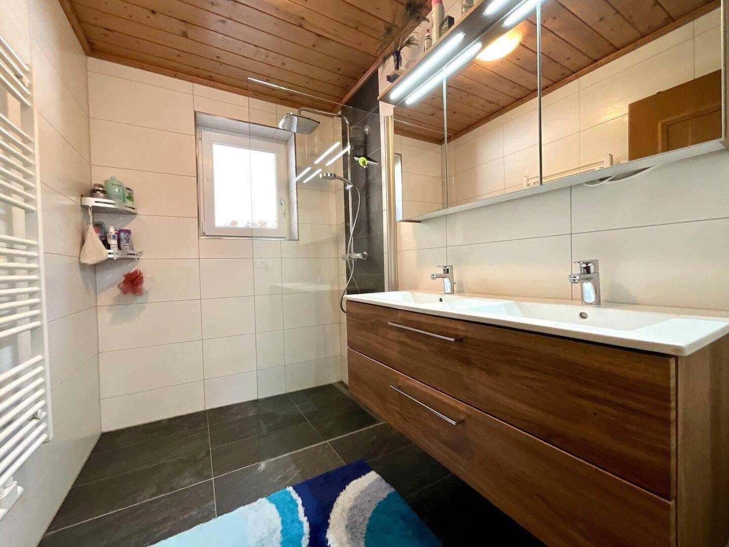 Modernes Badezimmer mit Doppelwaschbecken, Dusche und beheiztem Handtuchhalter.
