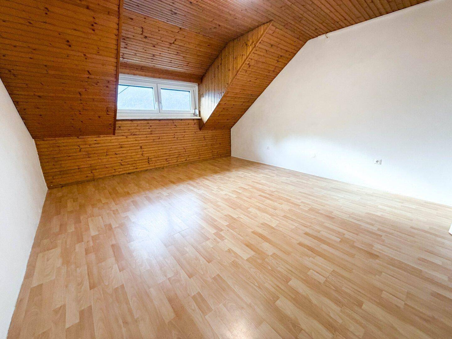 Geräumiges Zimmer im Dachgeschoss mit Laminatboden, Holzverkleidung und einem Fenster.