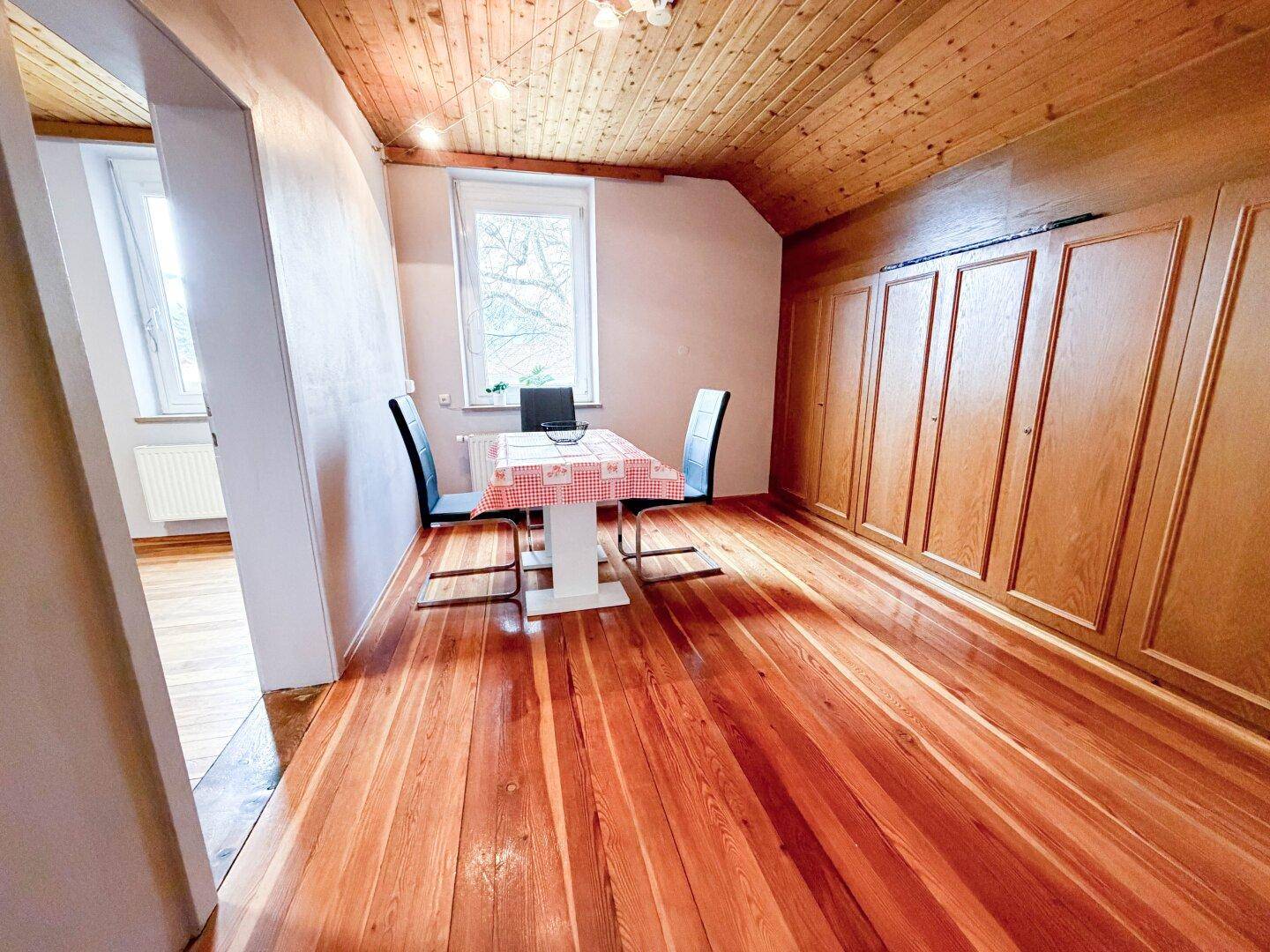 Essbereich im Dachgeschoss mit Holzboden, Holzdecken und Einbauschränken, hell durch Fenster.