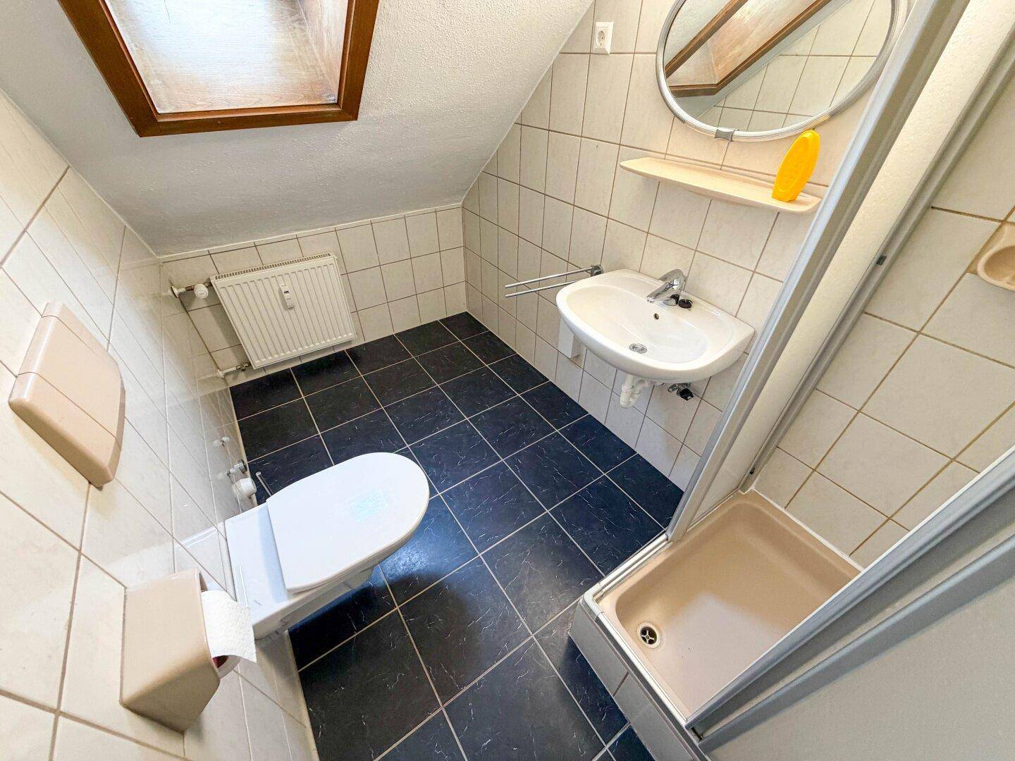 Kleines Badezimmer mit Dusche, WC und Waschbecken, ausgestattet mit dunklen Bodenfliesen.