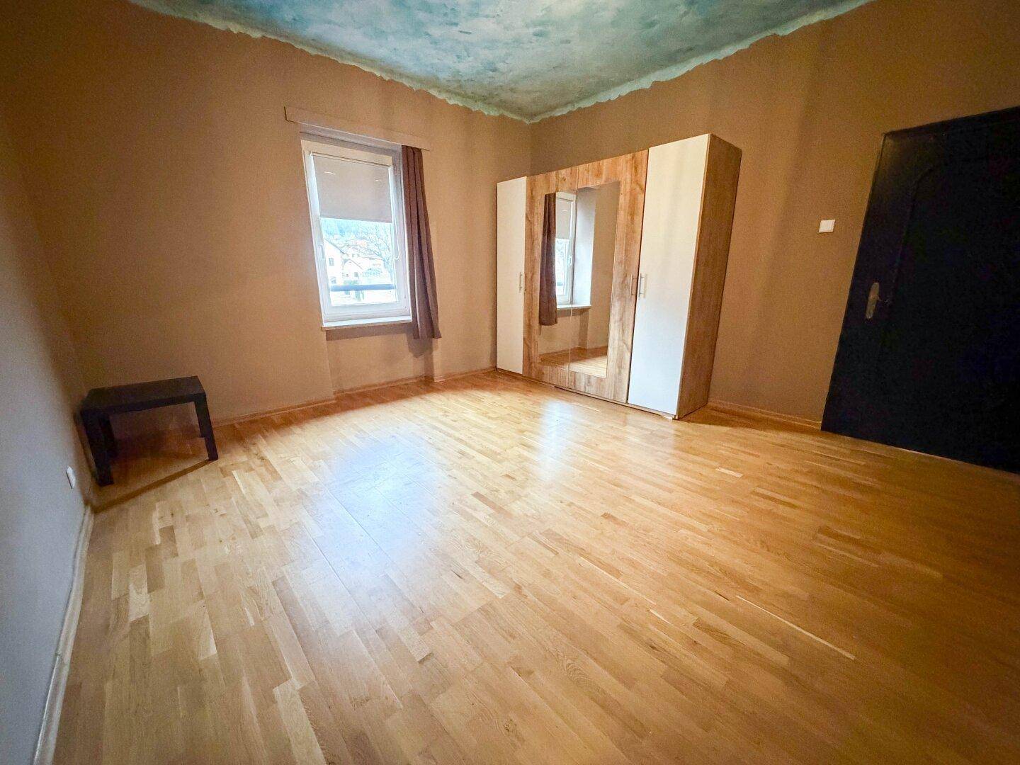 Geräumiges Schlafzimmer mit Laminatboden, Kleiderschrank und Fenster, hell und einladend.