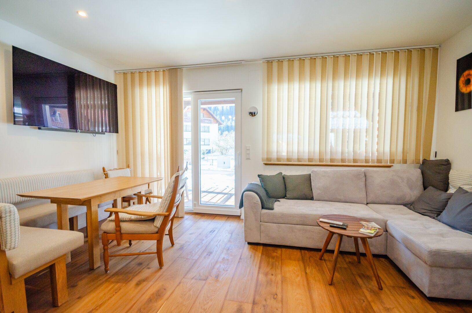 Gemütlicher Wohn-Essbereich mit Ecksofa, Holztisch und Zugang zu einem Balkon oder einer Terrasse.