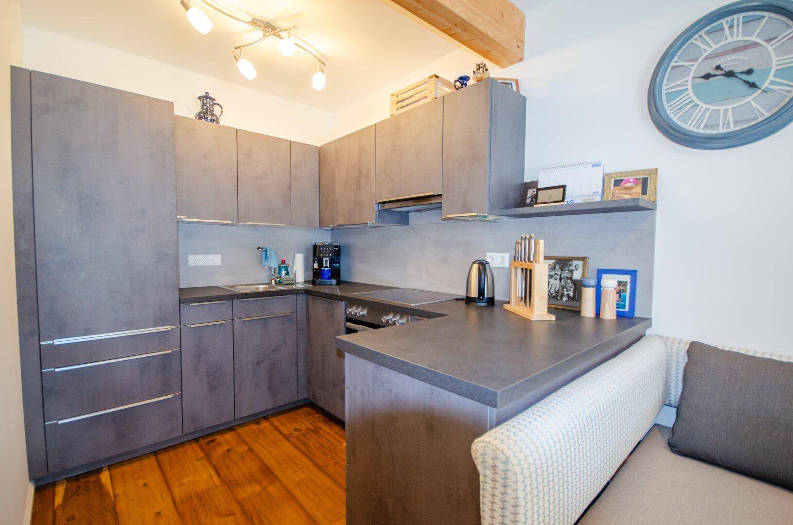 Moderne Küche mit grauen Schränken, Arbeitsplatte und Holzboden, offen zum Wohnbereich.