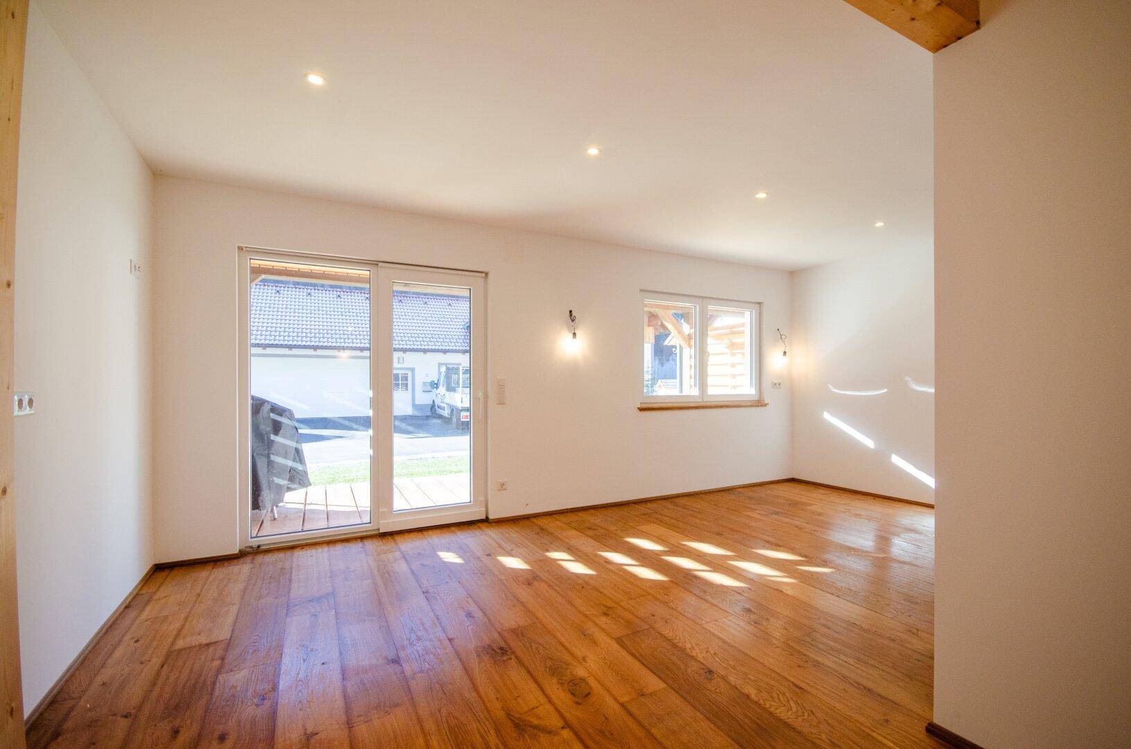 Lichtdurchfluteter Raum mit Holzboden, weißen Wänden und großem Schiebetürzugang nach draußen.