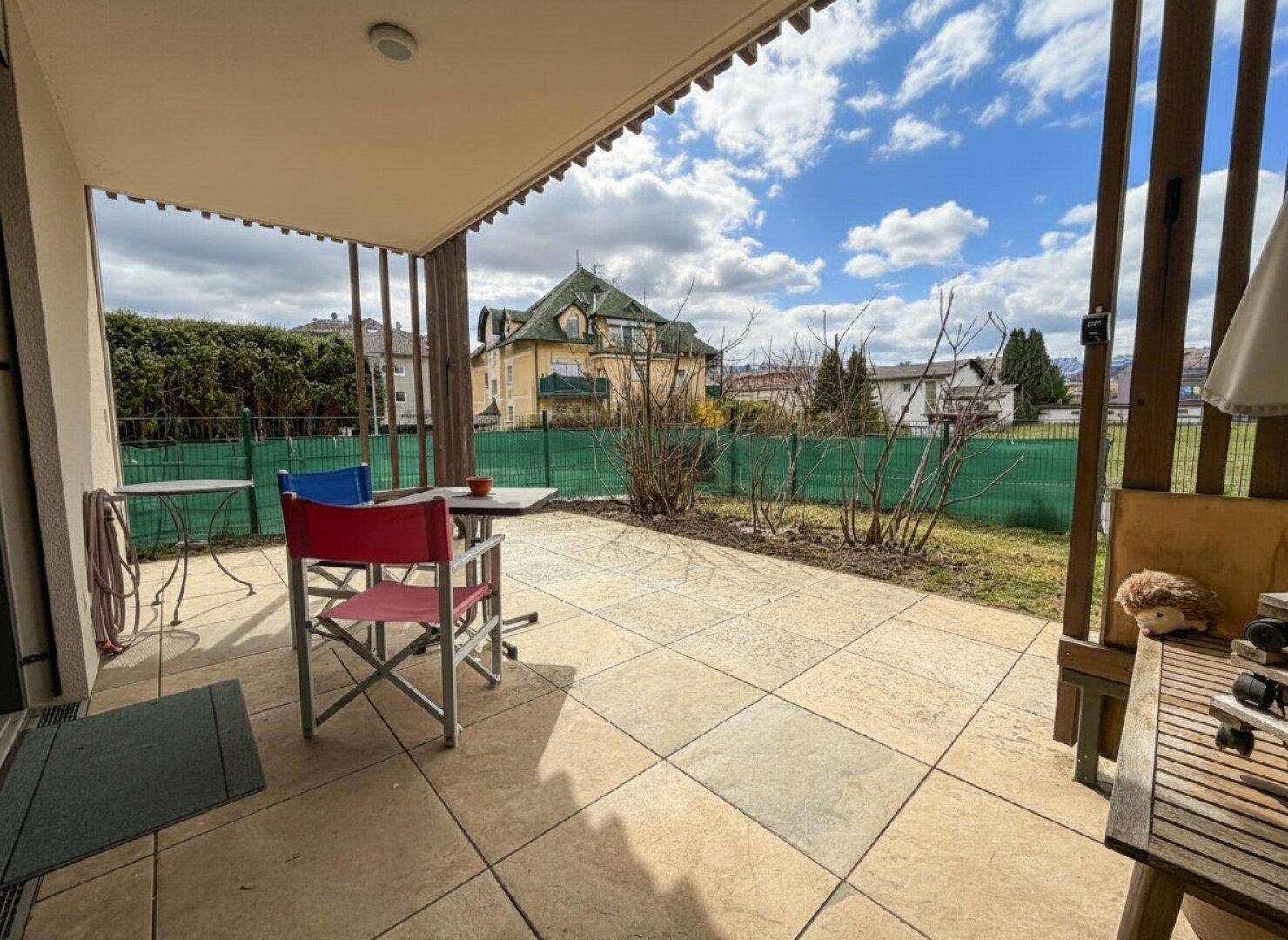 Überdachte Terrasse mit Sitzgelegenheiten und Blick auf ein charmantes Nachbargebäude.