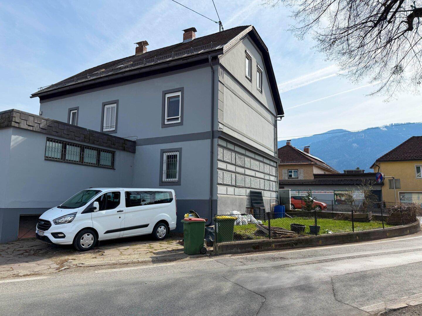 Seitenansicht des Gebäudes mit Parkplatz und einem kleinen Gartenbereich im ländlichen Umfeld.