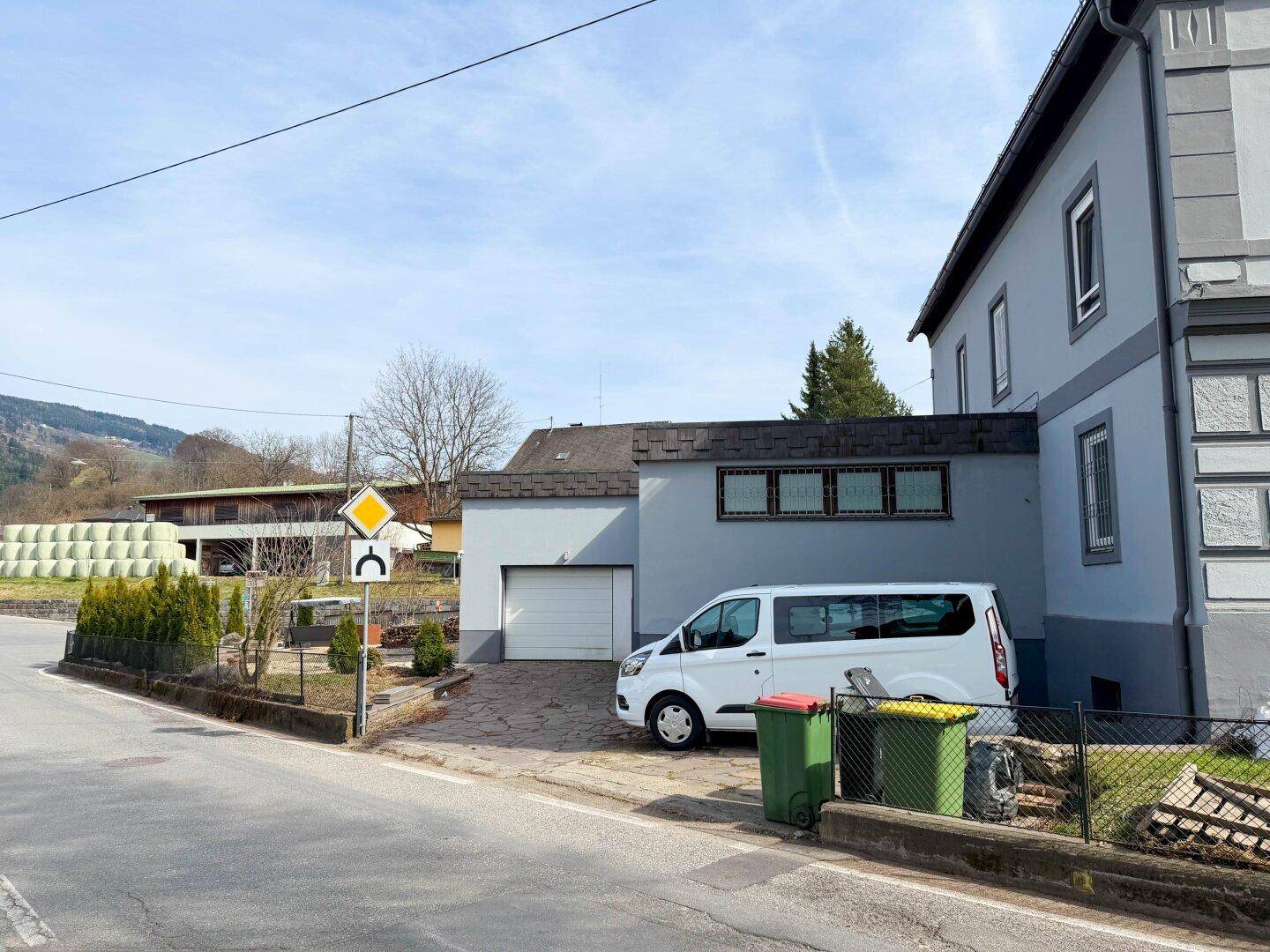 Rückansicht des Gebäudes mit Garage, Parkplatz und Blick auf die ländliche Umgebung.