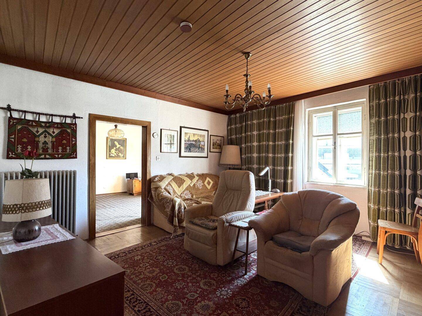Wohnzimmer mit Holzdecke, bequemen Sesseln, Sofa und traditionellen Vorhängen.