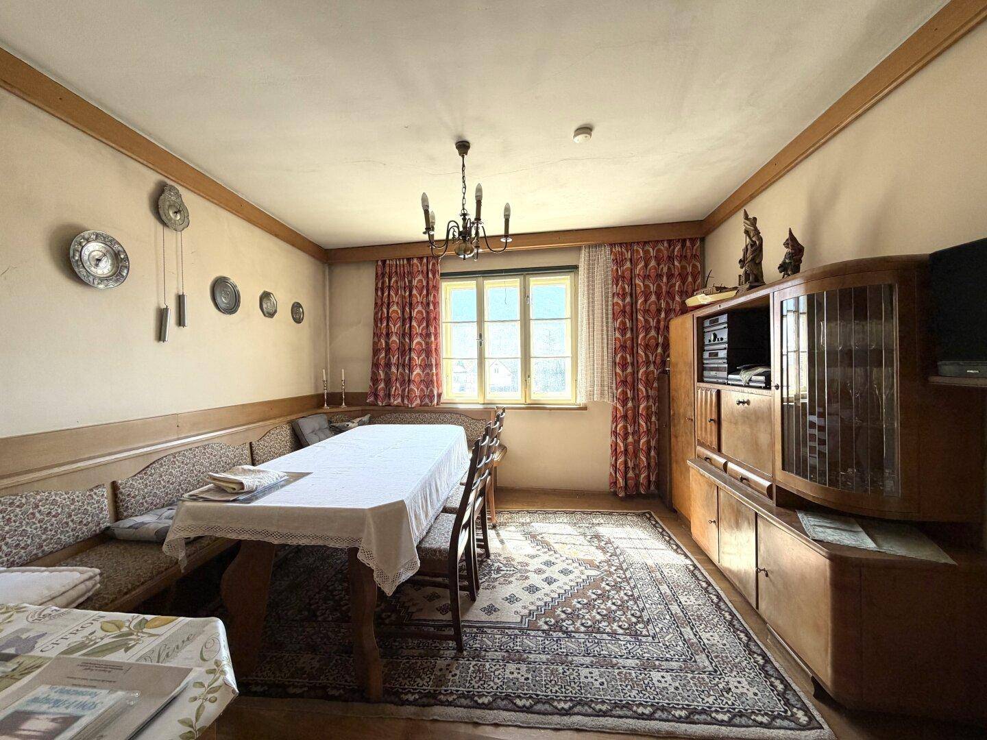 Gemütlicher Essbereich mit langem Tisch, eingebauter Sitzbank, Teppich und traditioneller Einrichtung.