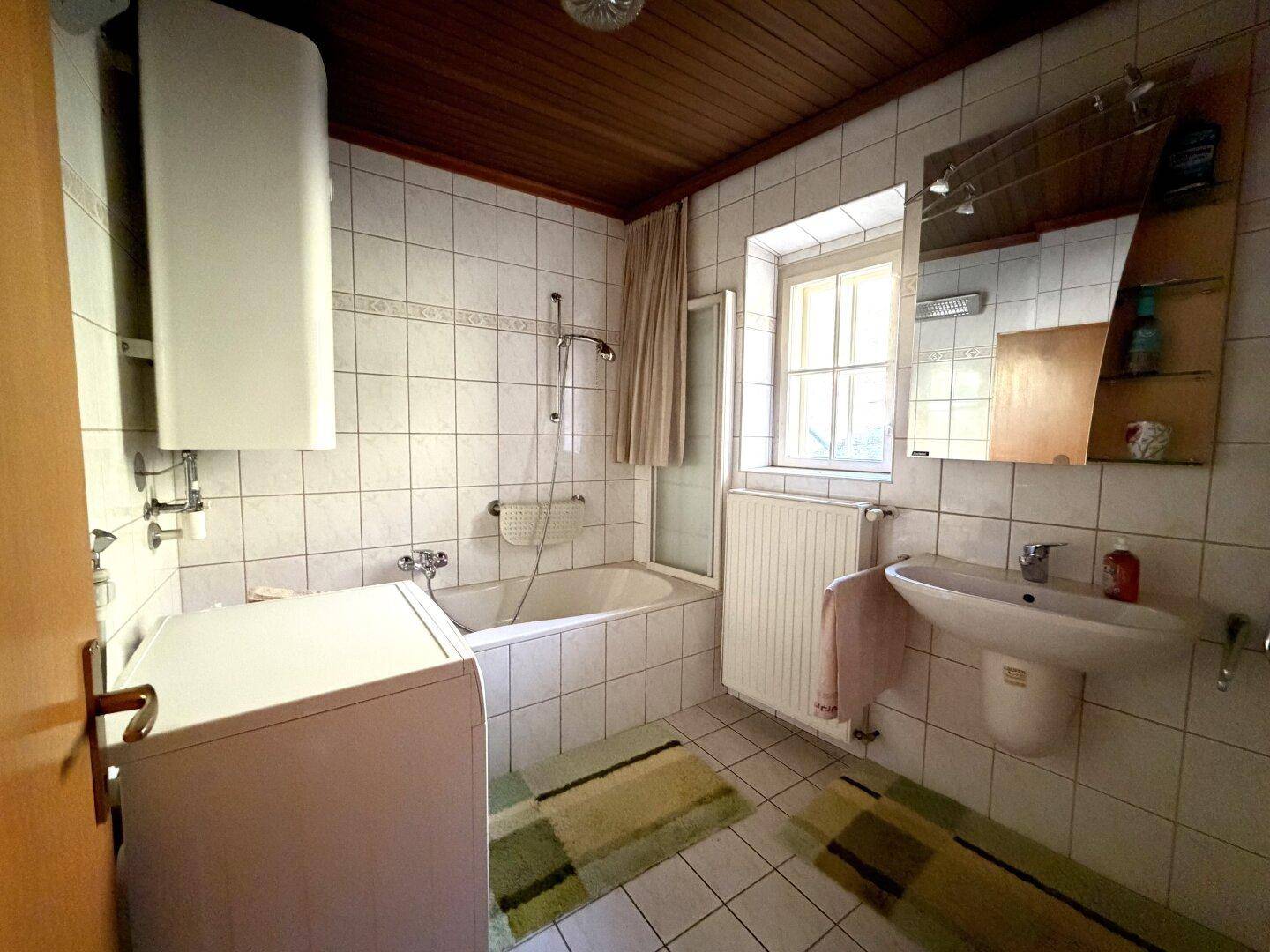 Gefliestes Badezimmer mit Badewanne, Duschvorrichtung, Waschbecken und Fenster für Tageslicht.