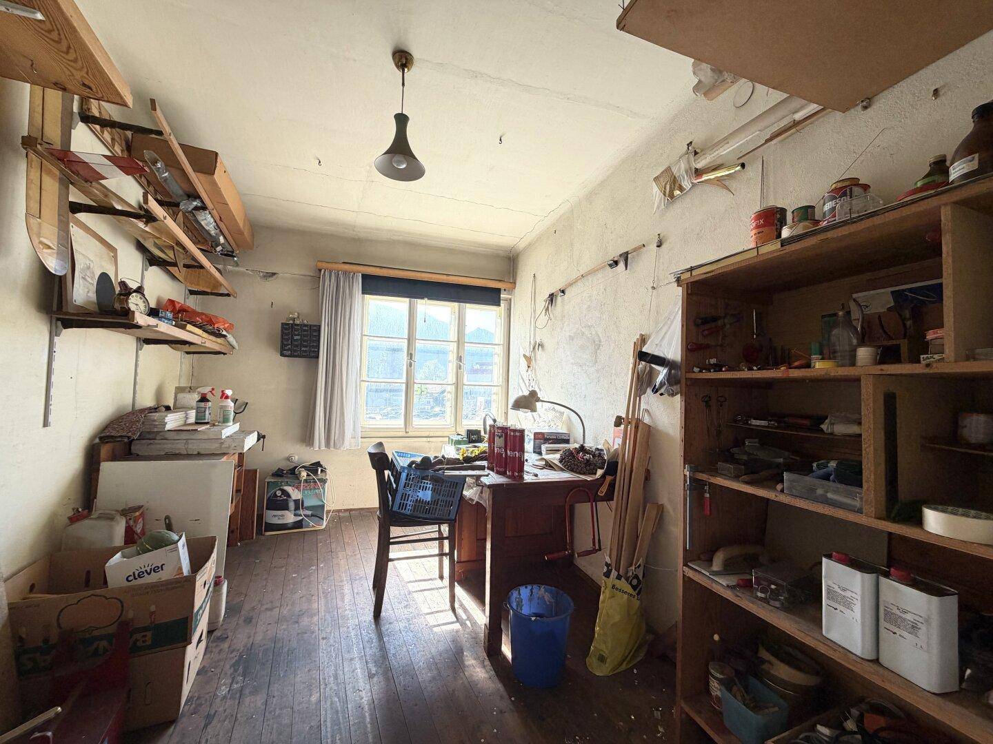 Helles Arbeitszimmer mit Holzboden, Schreibtisch, vielen Regalen und Blick ins Grüne.