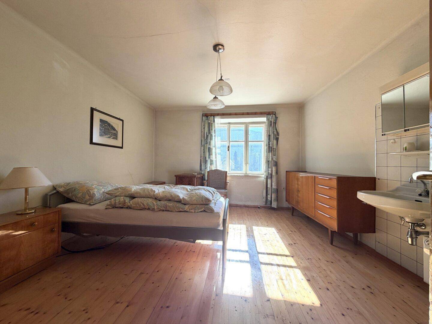 Helles Schlafzimmer mit Holzboden, Einzelbett, Vintage-Möbeln und einem integrierten Waschbecken.