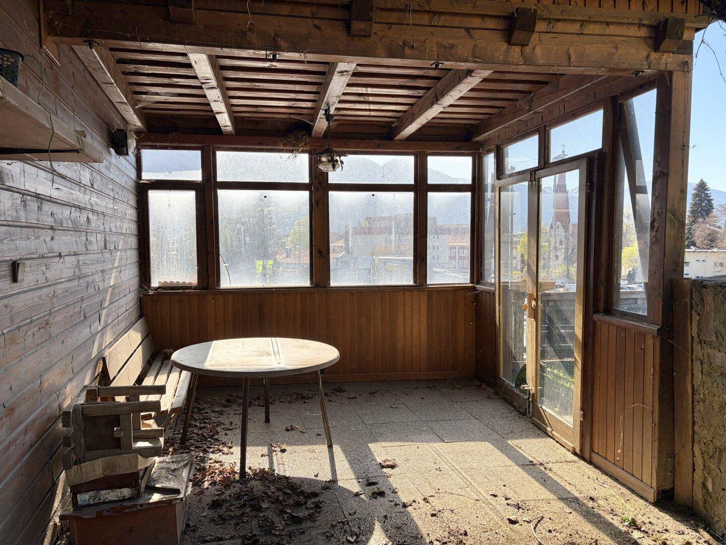 Überdachte Loggia mit Holzwänden, einem Tisch und Fenstern mit Blick auf die Umgebung.