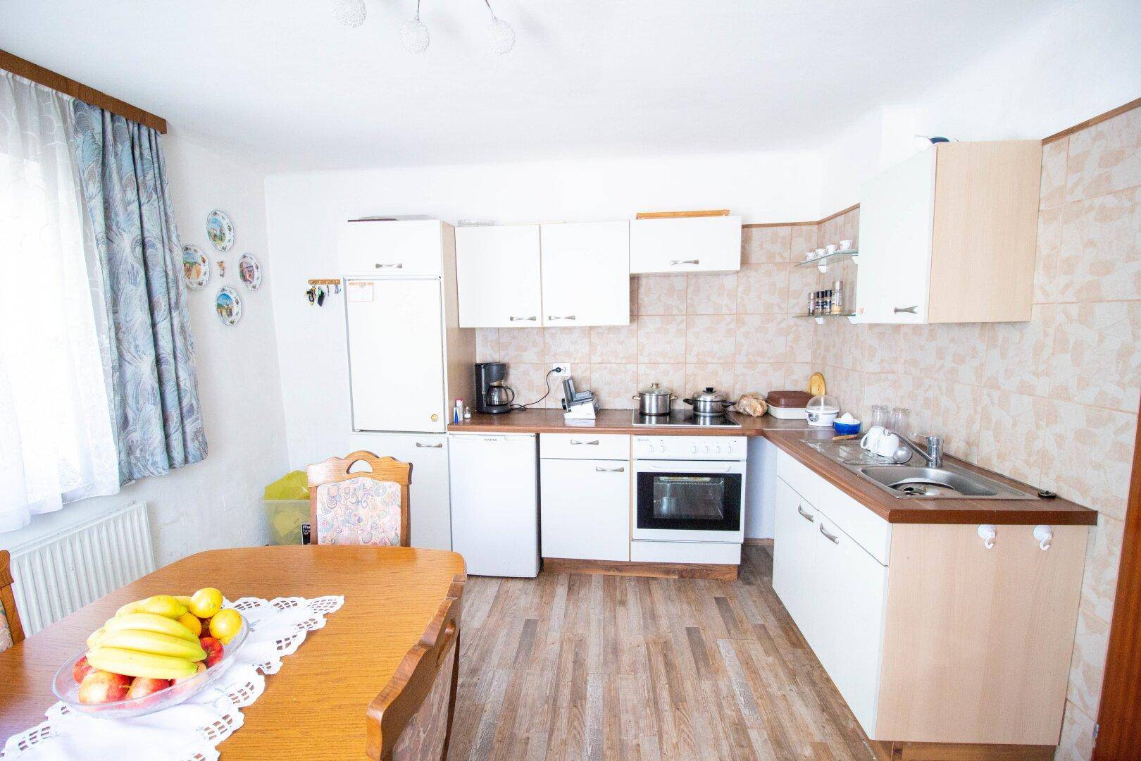 Funktionale Küche mit weißen Schränken, Essbereich und Blick nach draußen durch ein Fenster.
