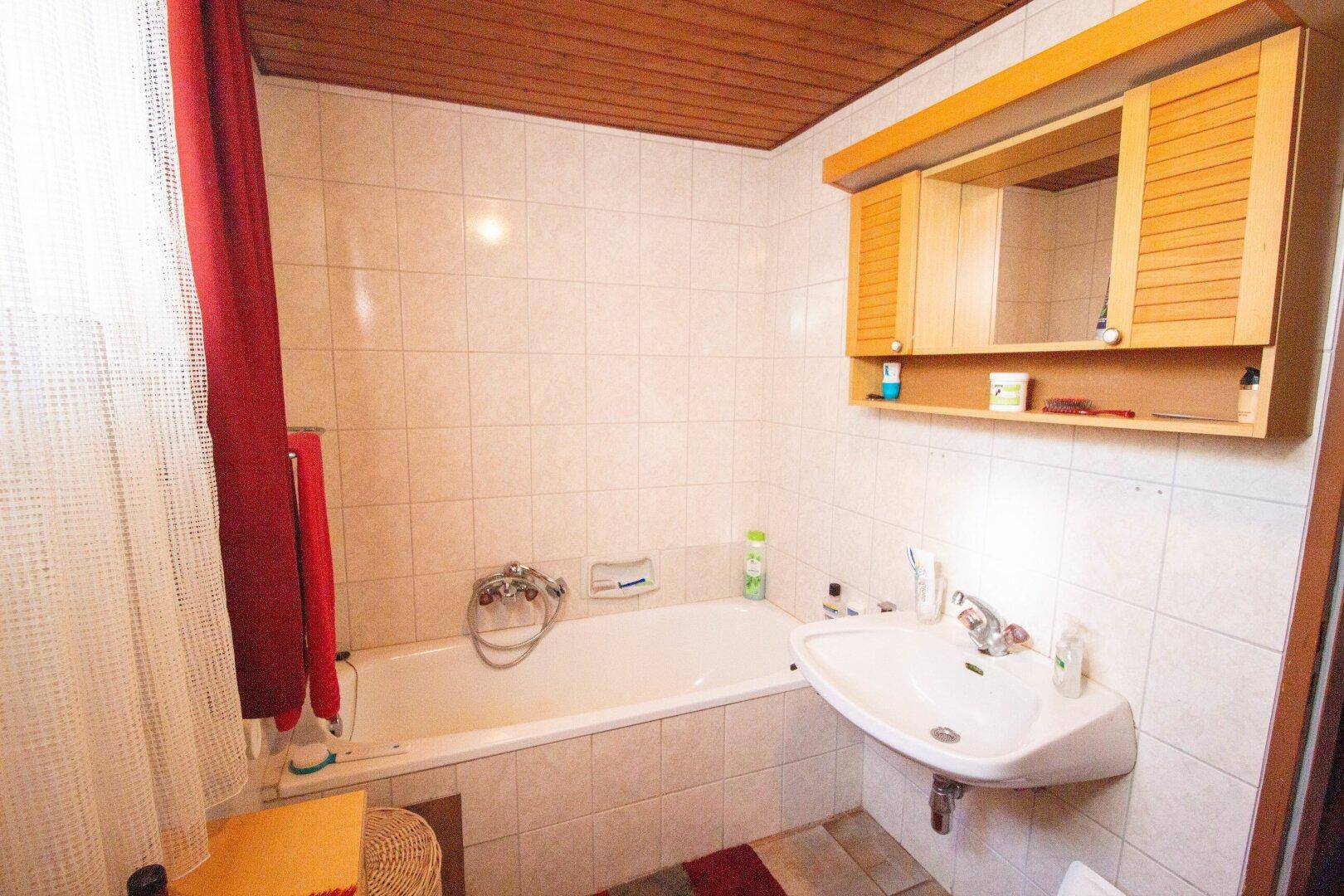 Traditionelles Badezimmer mit Badewanne, Waschbecken und Holzdecke, ausgestattet mit Fliesen.