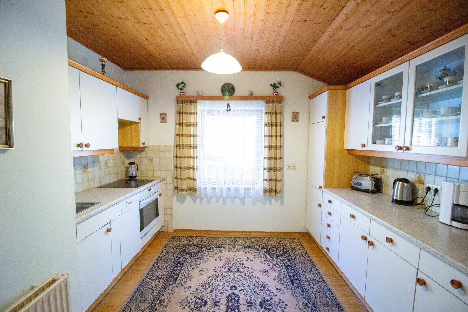Helle Küche mit weißen Schränken, Holzdecke und Teppich, ausgestattet mit modernen Geräten.