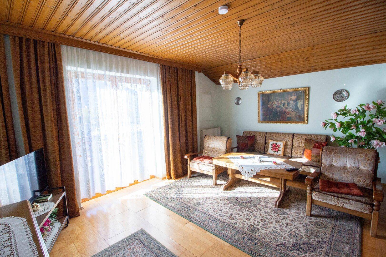 Traditionelles Wohnzimmer mit Holzdecke, bequemen Sofas und Zugang zu einem Balkon.