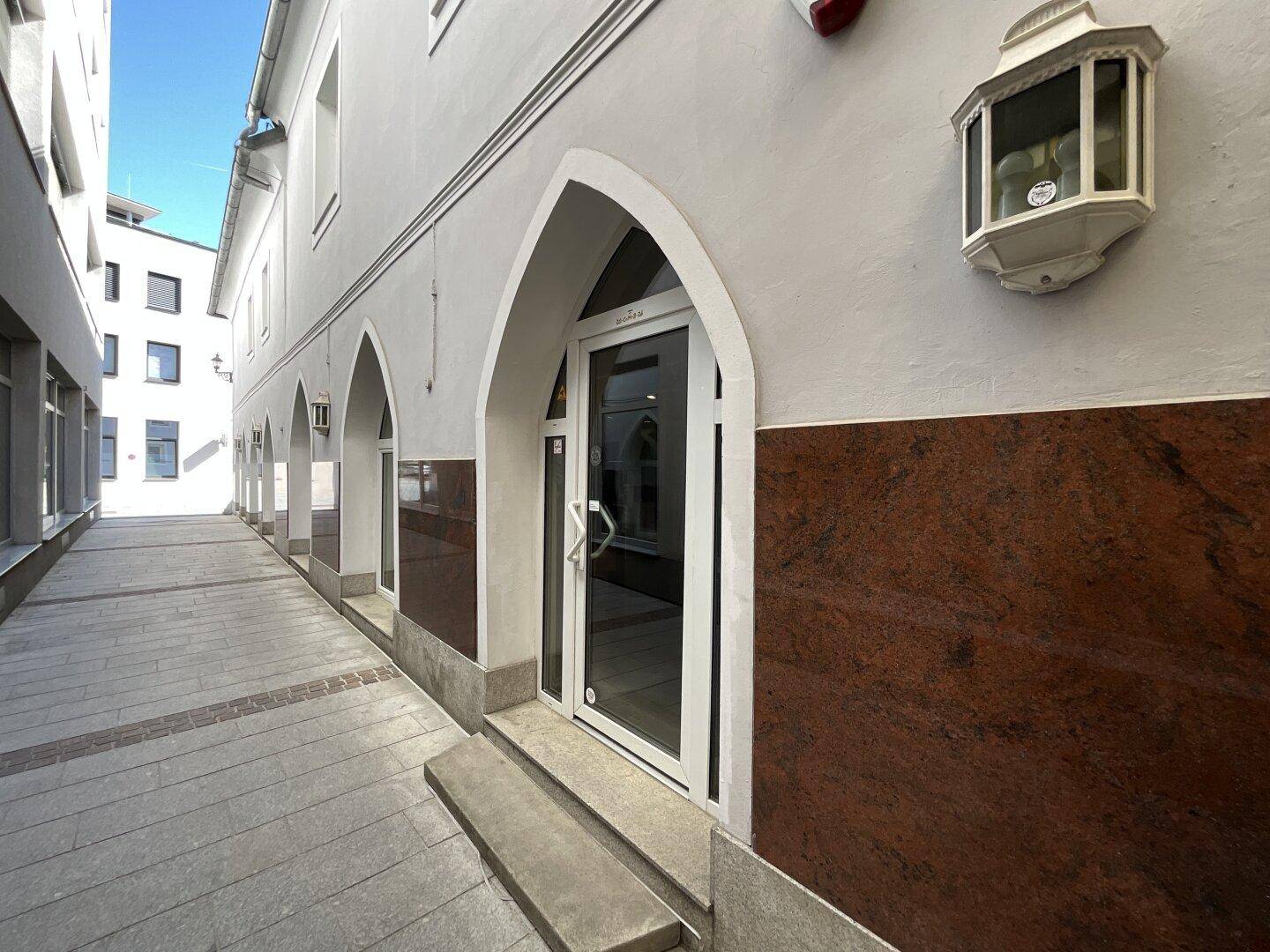 Gebäudeeingang in einer Gasse mit gewölbter Tür und roter Granitverkleidung.