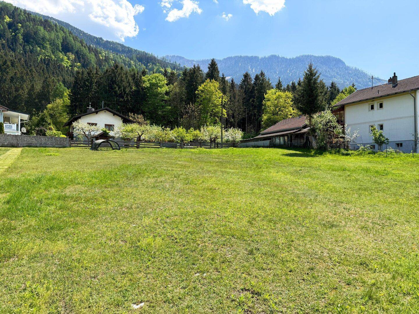 Idyllische grüne Landschaft mit weitem Blick auf bewaldete Hügel und vereinzelte Gebäude.