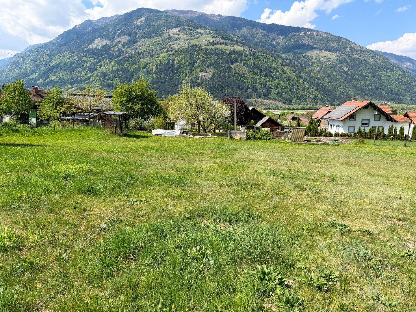 Offene Wiesenfläche mit Panoramablick auf eine große Bergkette und ländliche Bebauung.