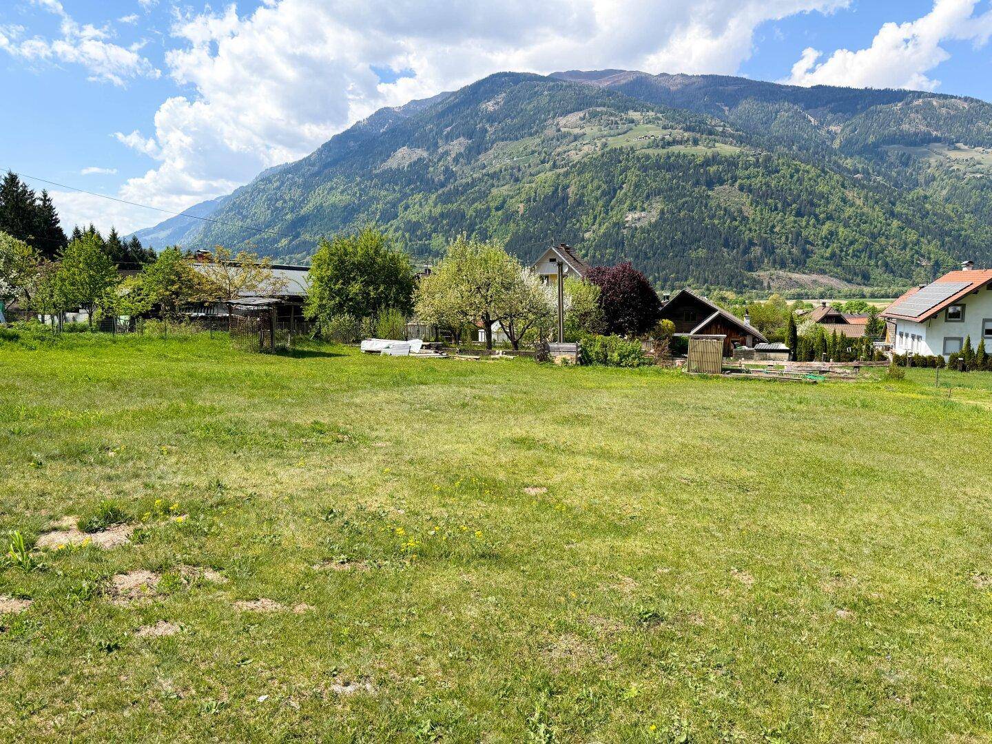 Weitläufige Wiesenlandschaft mit Blick auf die majestätischen Berge und einige Häuser.