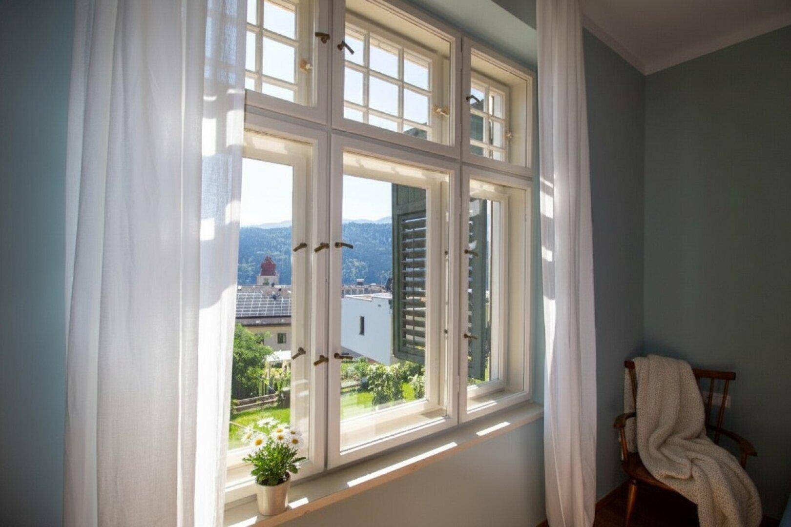 Fenster mit Blick auf die umliegende Landschaft, Dächer mit Solaranlagen und den See.