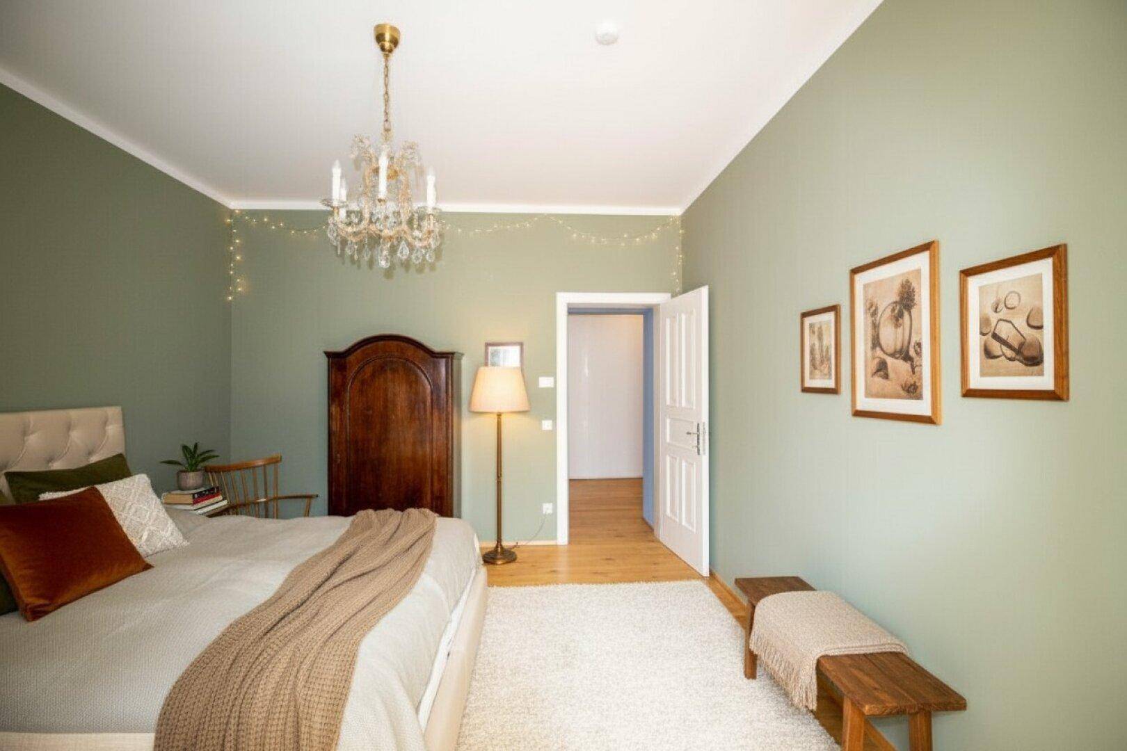 Gemütliches Schlafzimmer mit grünen Wänden, Holzboden und einem großen Bett mit bequemer Decke.