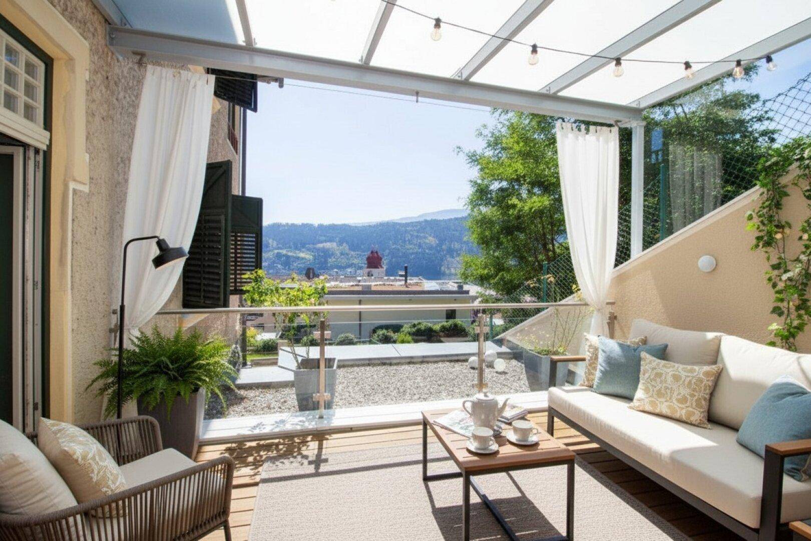 Überdachte Terrasse mit bequemen Outdoor-Möbeln und weitem Blick über die Stadt und den See.