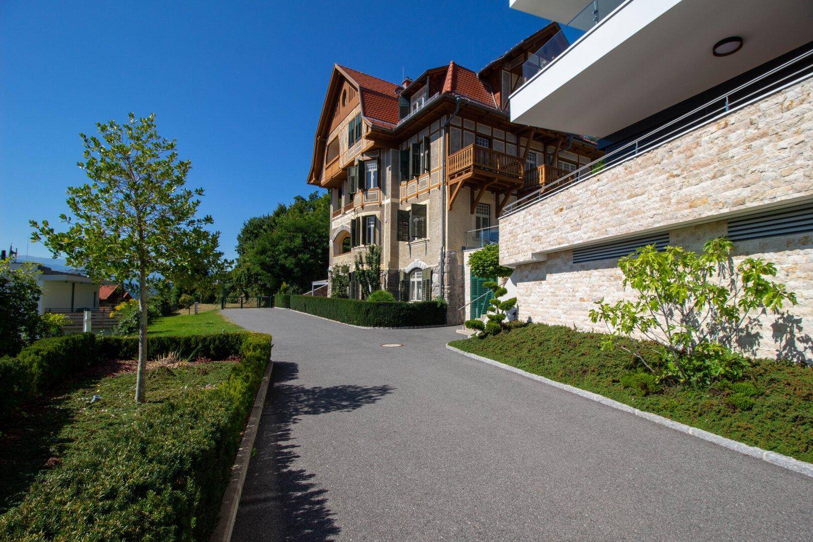 Zufahrt zur historischen Villa mit gepflegter Hecke und umgebender grüner Landschaft.
