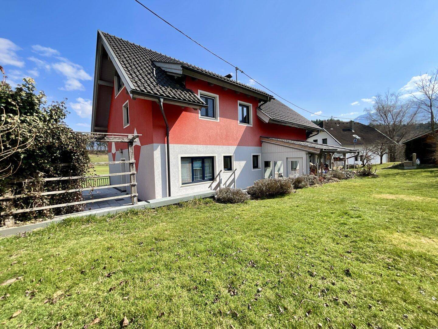 Seitenansicht des Hauses mit roter Fassade, dunklem Ziegeldach und gepflegtem Gartenbereich.
