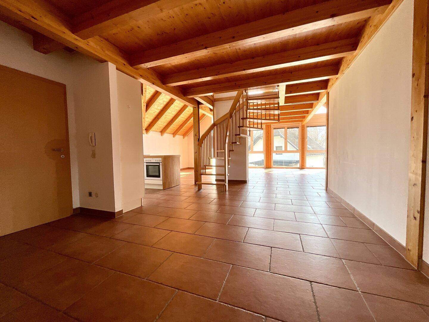 Geräumiger Wohnbereich mit Terrakottafliesen, sichtbaren Holzbalken und einer eleganten Wendeltreppe.