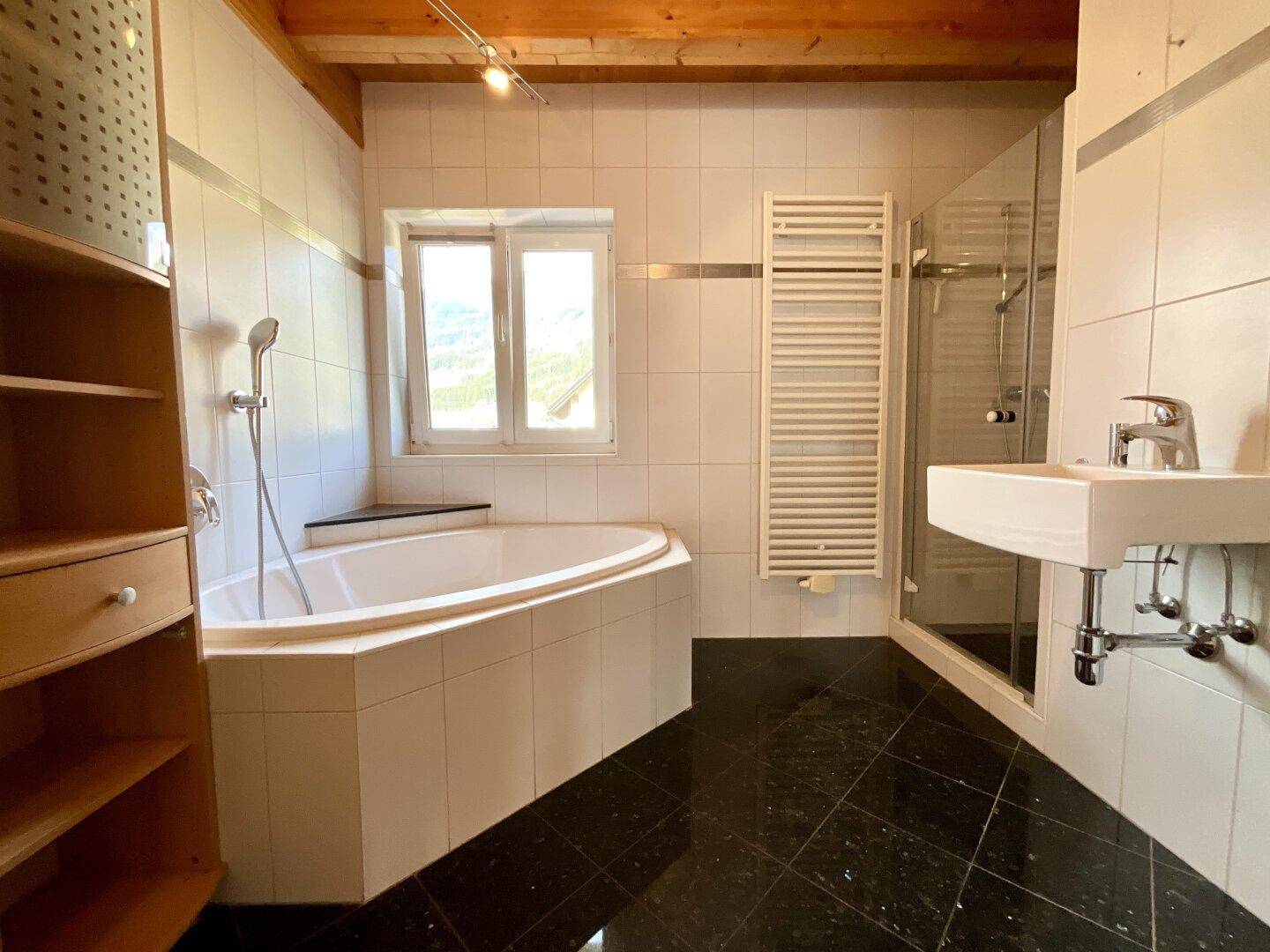 Modernes Badezimmer mit schwarzen Fliesen, Eckbadewanne, Duschkabine und beheiztem Handtuchhalter.