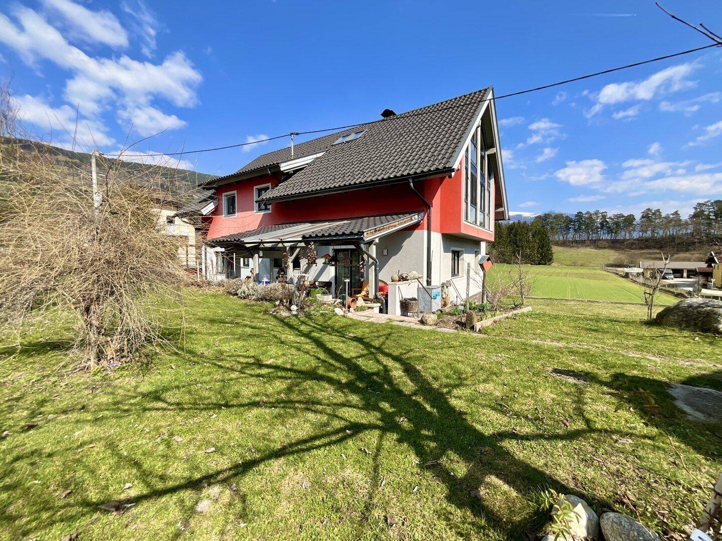 Seitenansicht des Hauses mit roter Fassade, dunklem Ziegeldach und weitläufigem Gartenbereich.