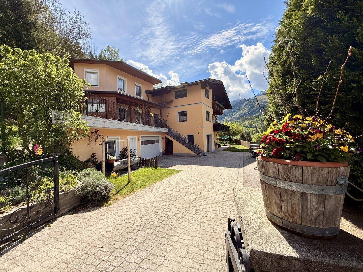 Großzügige Auffahrt zum Haus mit gepflastertem Bereich und blühenden Pflanzen.