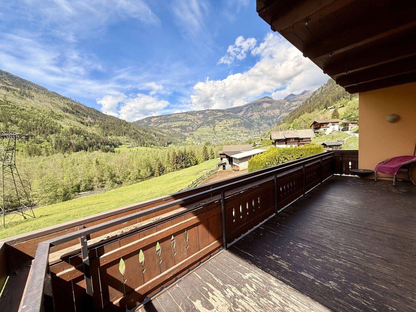 Geräumiger Balkon mit Holzboden und weitem Blick über das Tal und die Berge.