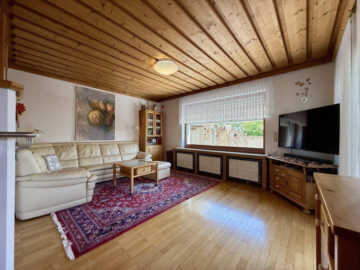Geräumiges Wohnzimmer mit Holzdecke, bequemer Ledercouch und traditionellem Teppich.