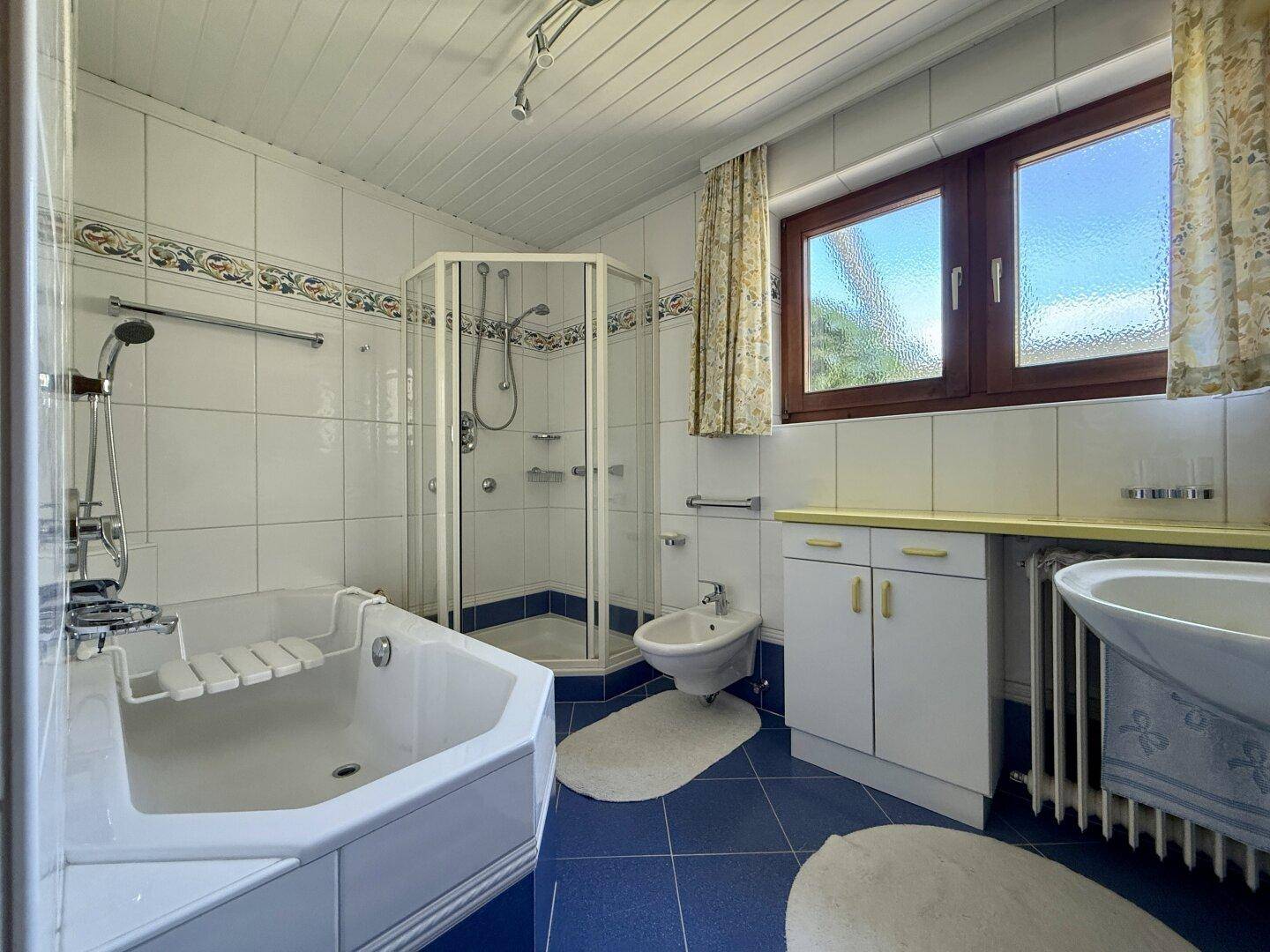 Badezimmer mit blauen Fliesen, Badewanne, Duschkabine und Fenster.
