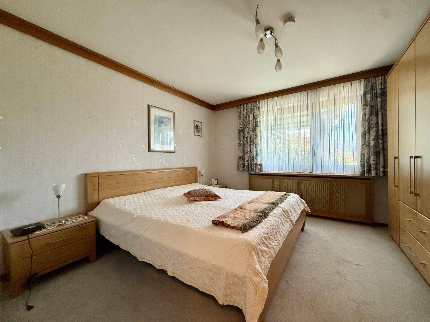 Helles Schlafzimmer mit Doppelbett, Teppichboden und Holzmöbeln im traditionellen Stil.